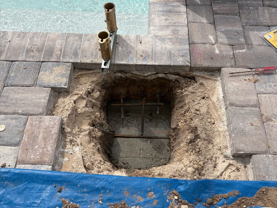 Pavers lifted next to the pool with a rebar-reinforced concrete footing poured and two brass anchor sockets held in place